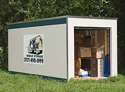 A Lok Box container on grass with its roll-up door open, showing stored boxes and furniture